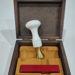 Sello de lacre blanco con una barra pequeña de lacre de color rojo, en un estuche de madera con el cierre en dorada
