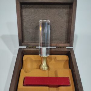 Sello de lacre de metacrilato con una barra pequeña de lacre de color rojo, en un estuche de madera con el cierre en dorada