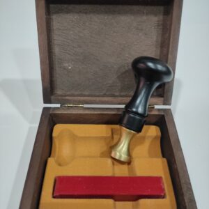 Sello de lacre negro con una barra pequeña de lacre de color rojo, en un estuche de madera con el cierre en dorada